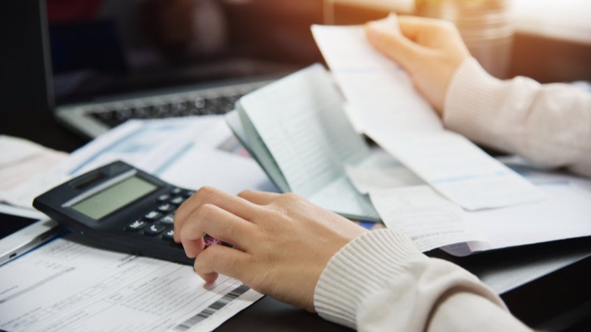 Nahaufnahme einer Person, die mit Taschenrechner, Belegen und Finanzdokumenten arbeitet.
