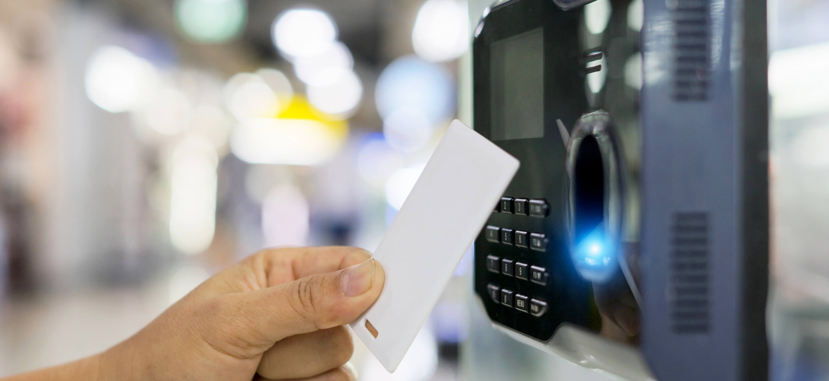 Nahaufnahme eines schwarzen Zeiterfassungsterminals. Man sieht eine Hand, die einen Badge in die Nähe des Terminals hält.