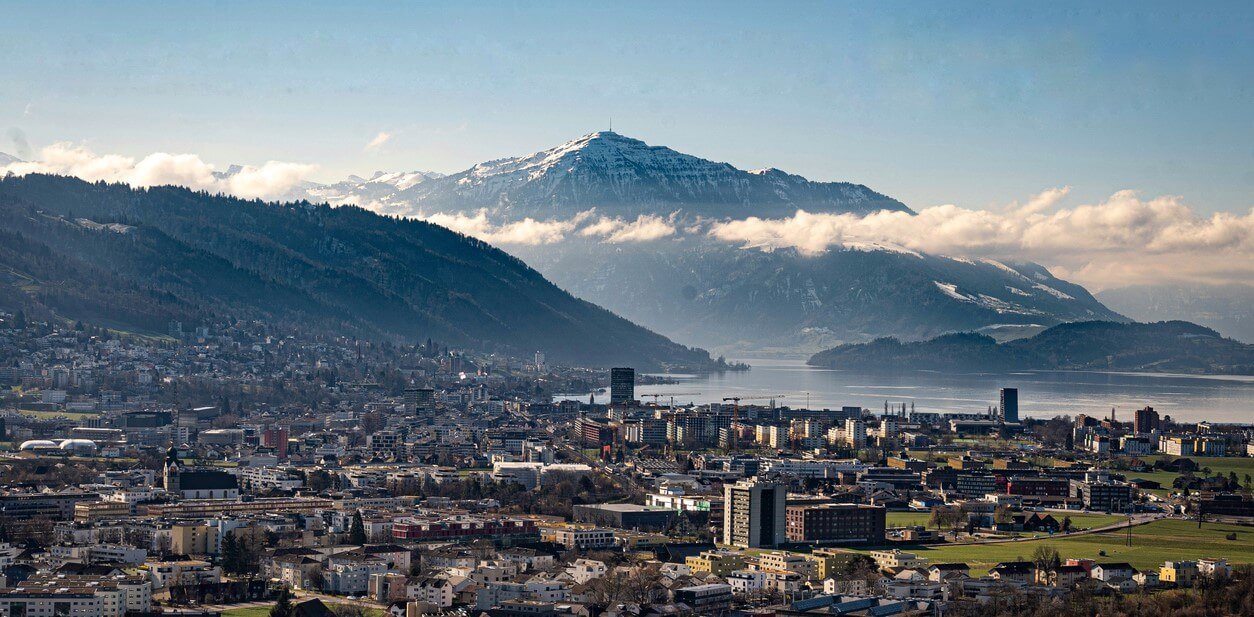 Bild der Stadt Zug: verschiedene Gebäude mit Blick auf See und Berge