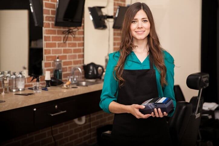 Abbildung einer Coiffeur-Mitarbeiterin, die ein Kartenterminal in der Hand hält